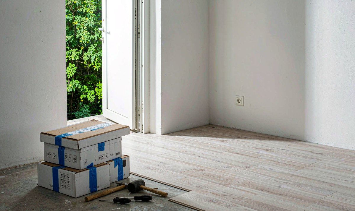 住宅房间内正在铺装浅色木地板,旁边放着未拆封的地板纸箱与工具